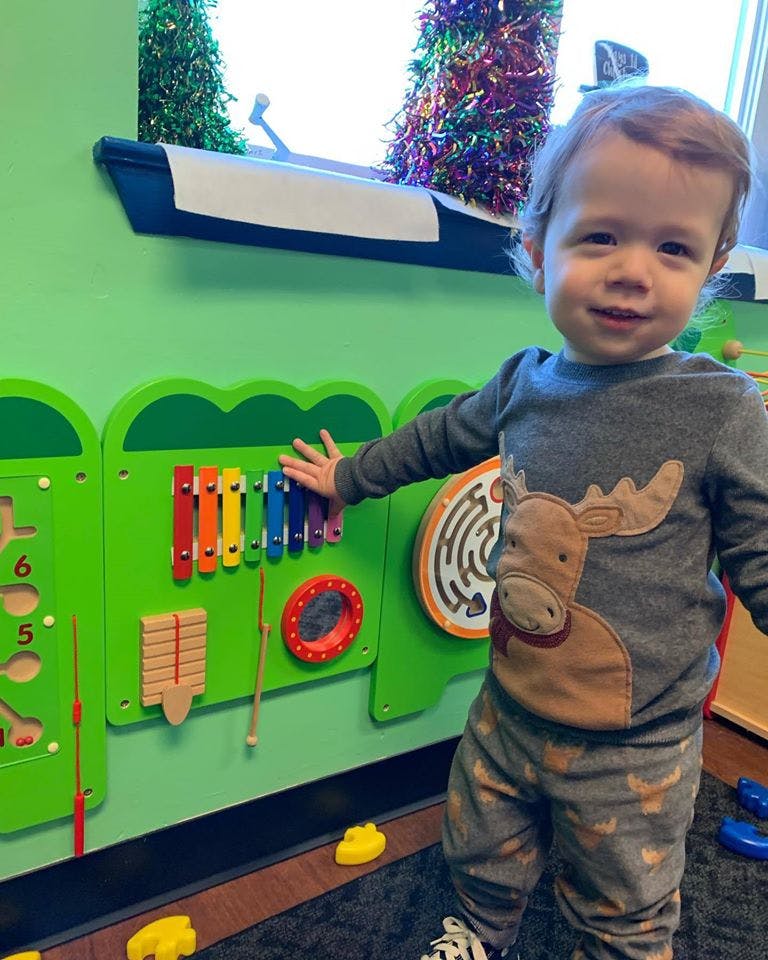 Child playing with a colorful xylophone on a green activity board