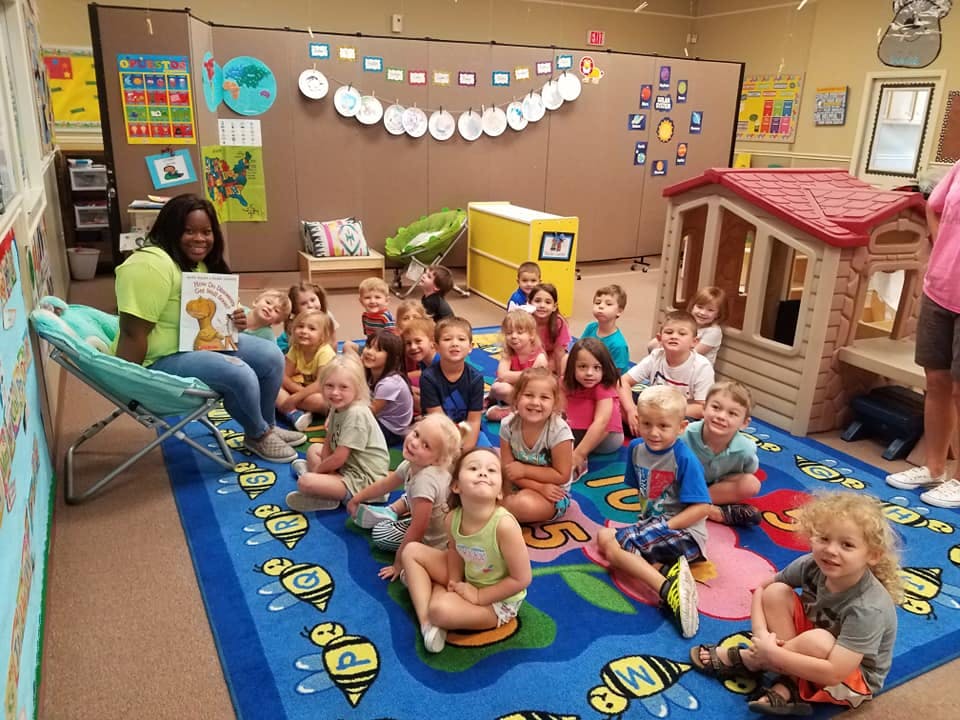 Person reading a book to a group of children in a classroom