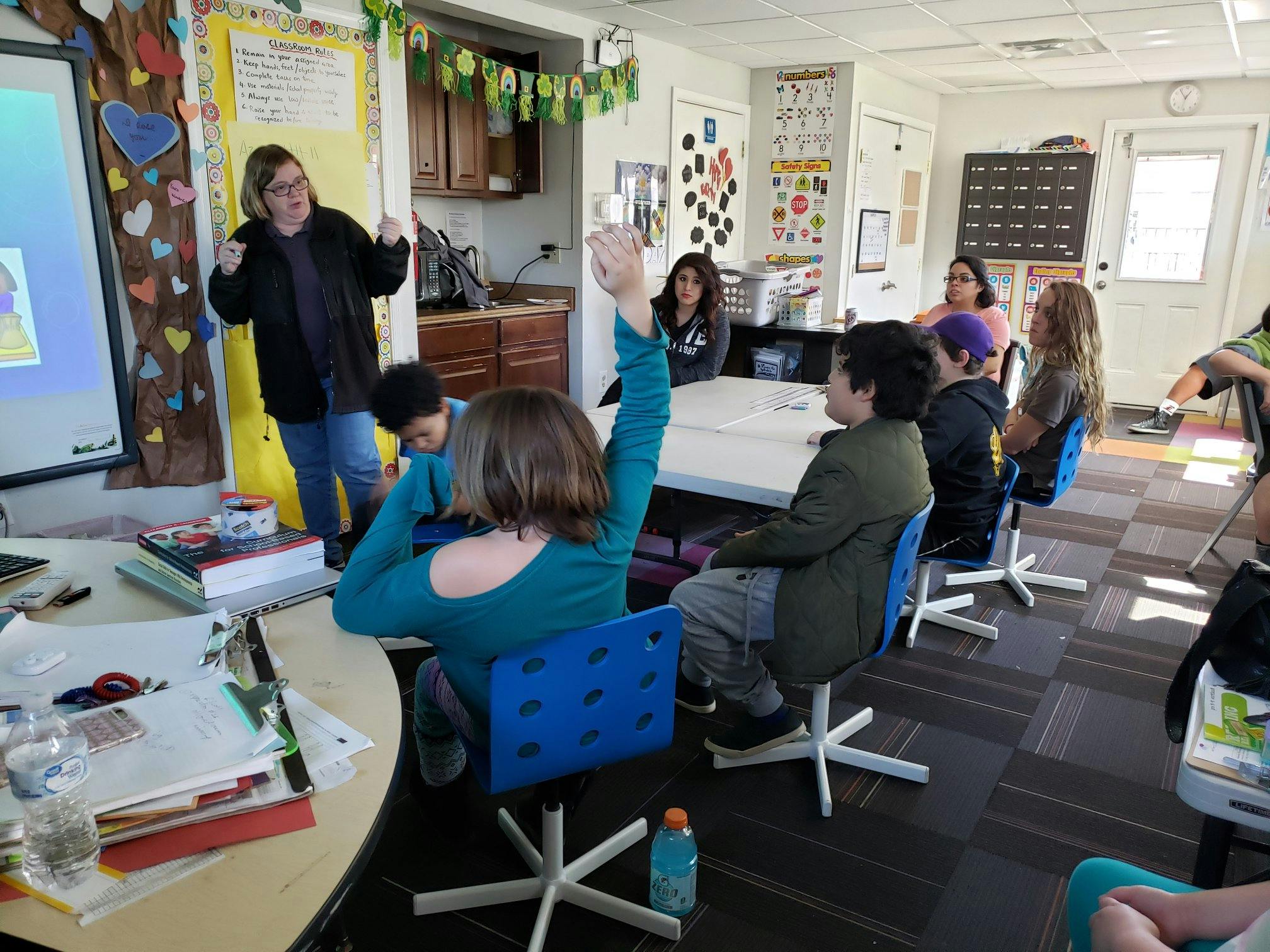 Person teaching a group of people in a classroom, one person raising a hand
