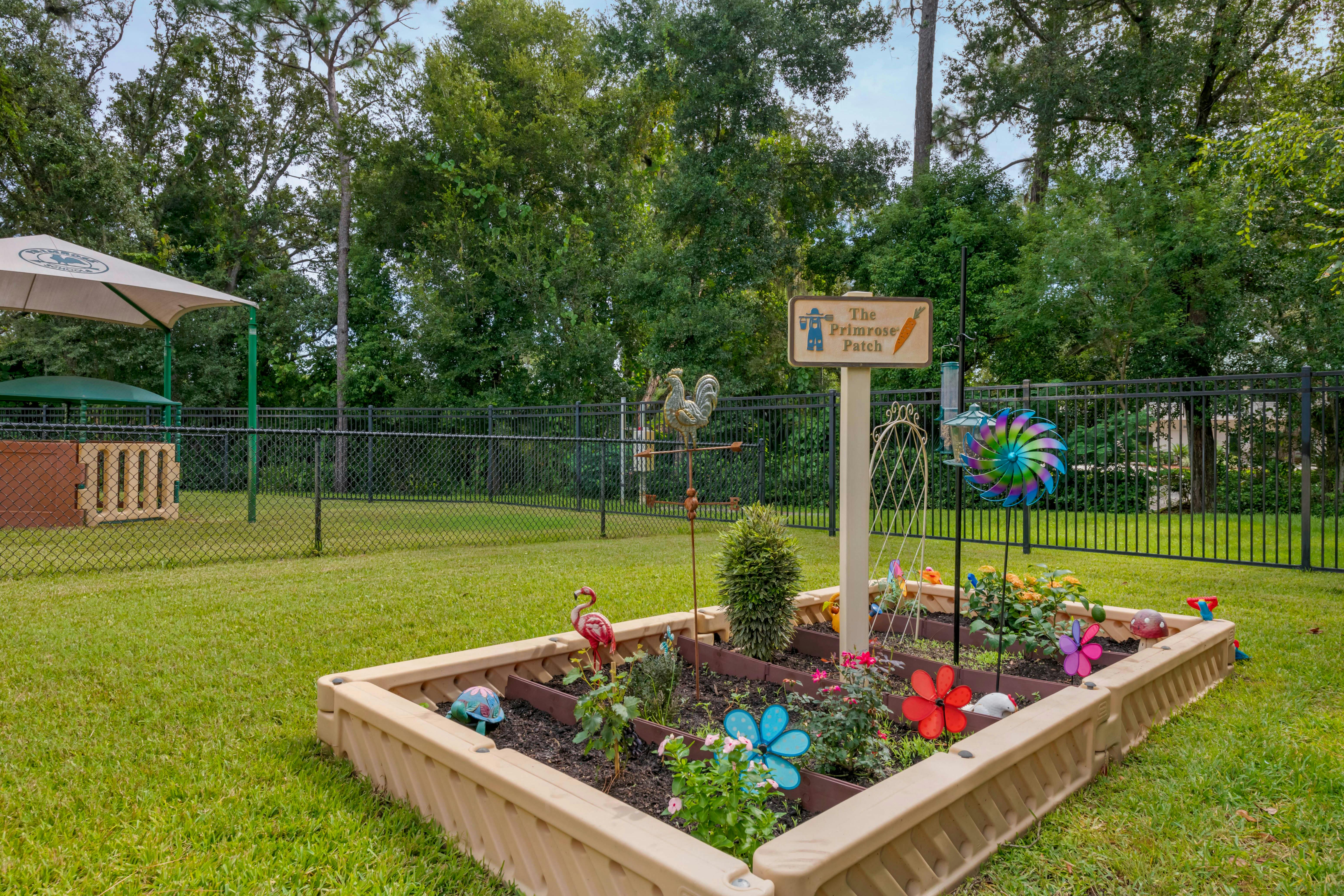 Raised garden bed with flowers and decor in a grassy yard next to a fence