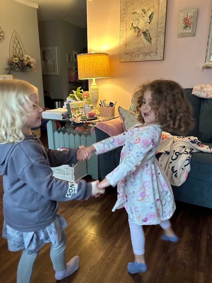 Two children holding hands and dancing in a living room