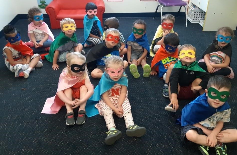 Group of children wearing superhero capes and masks sitting on the floor
