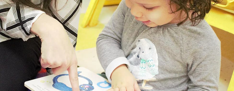 Person pointing at a book with a child looking at it