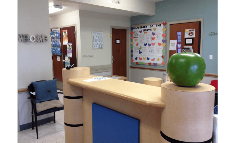 Reception desk with a large green apple sculpture in a room with a bulletin board