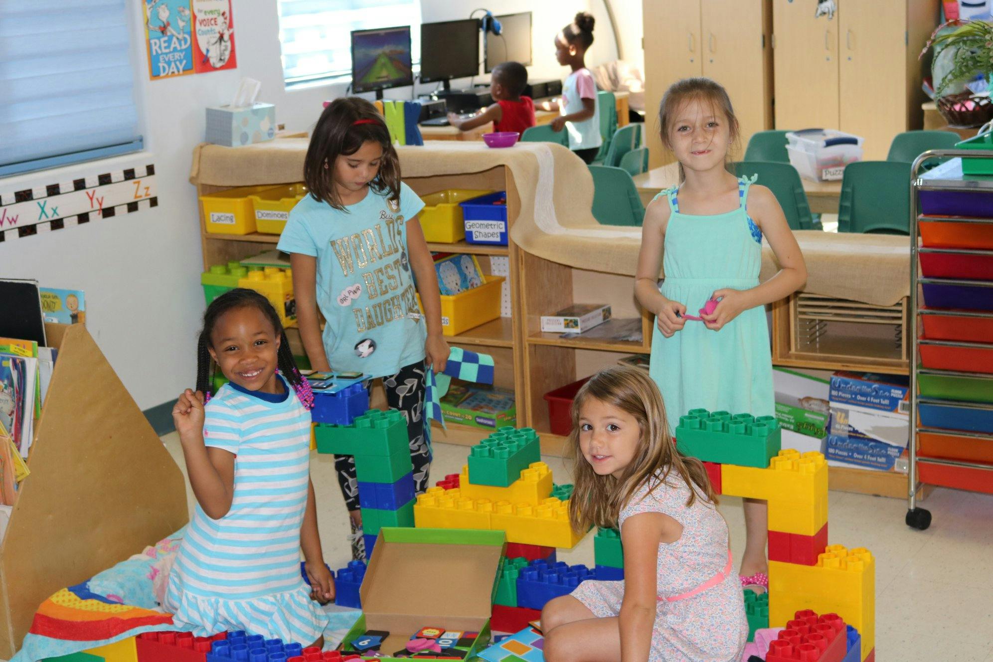 Four children playing with large building blocks in a classroom