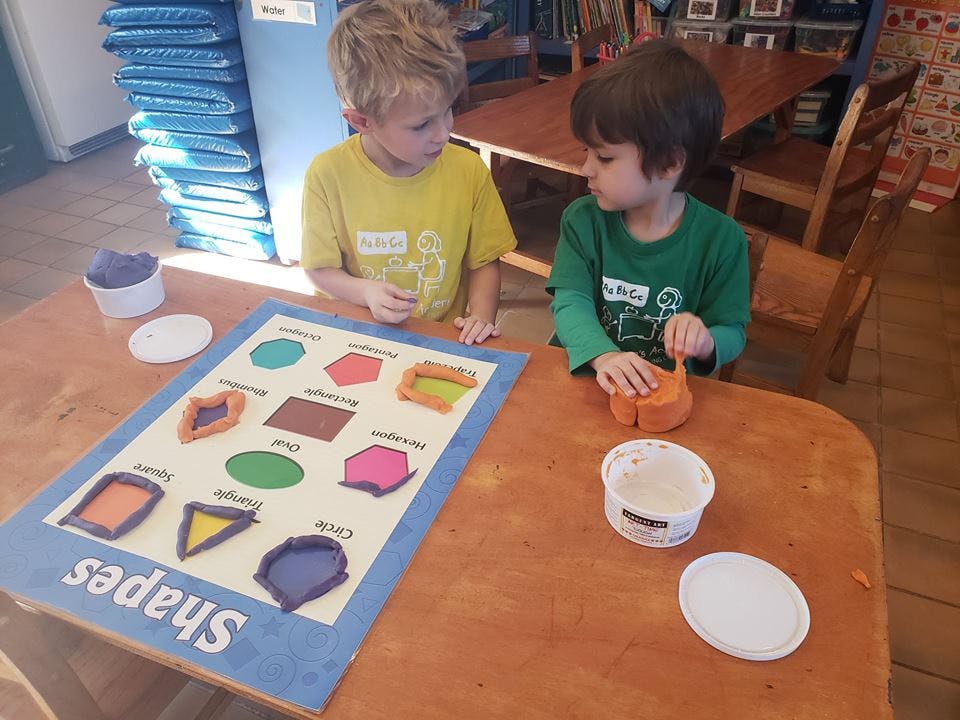 Two children playing with playdough and a shapes mat