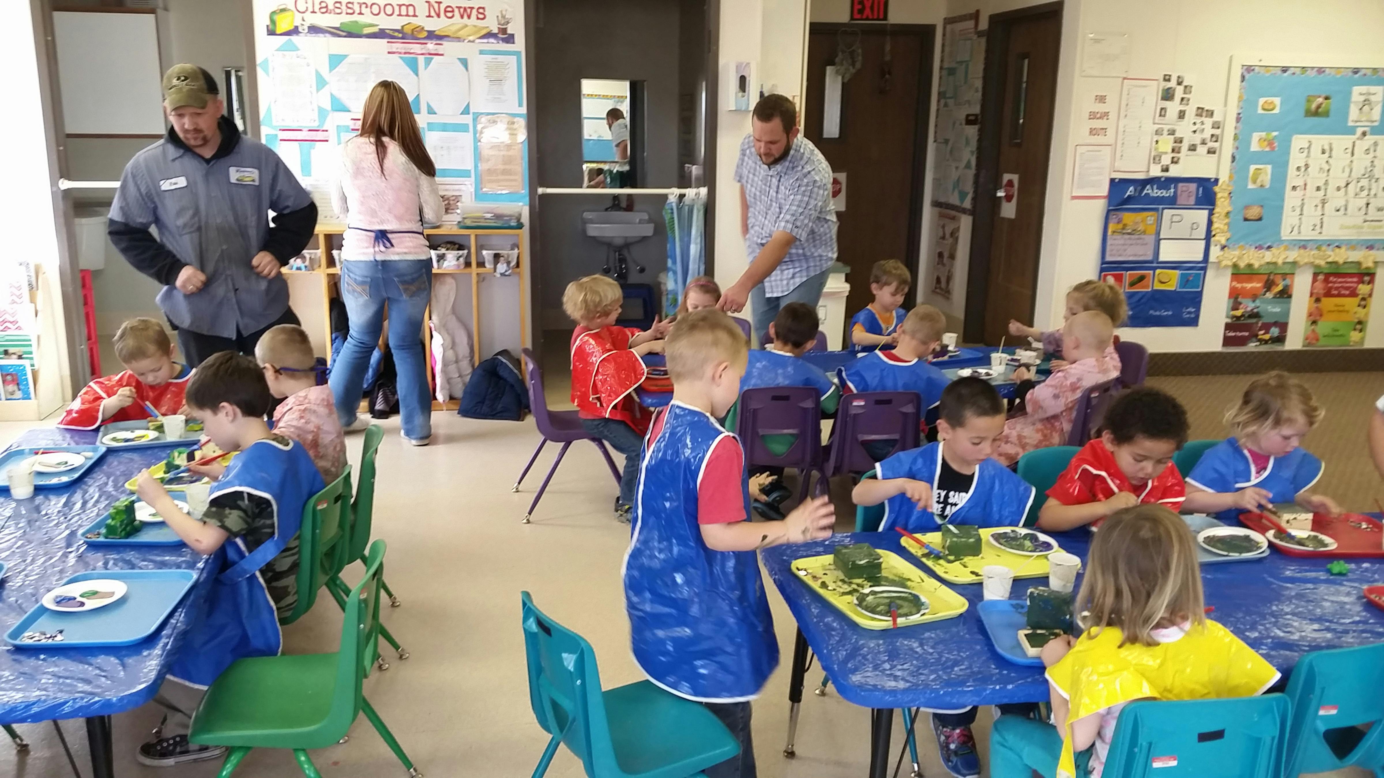 Adults supervising children at tables in a classroom