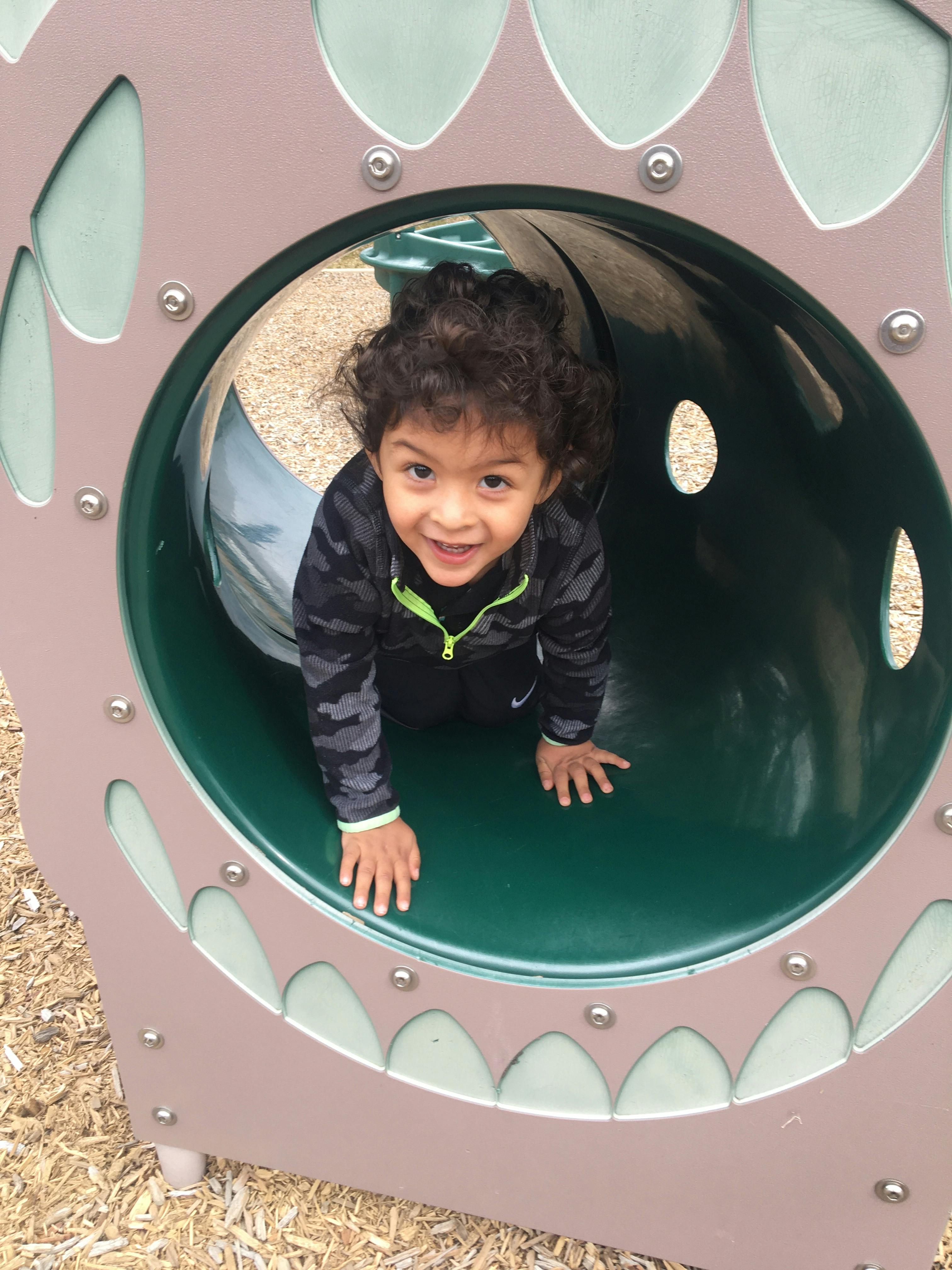 Child crawling through a green tunnel on a playground