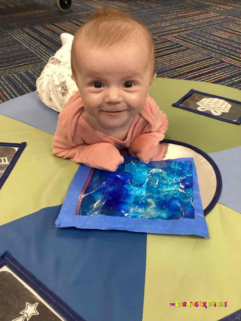 Baby on tummy time playing with a sensory bag
