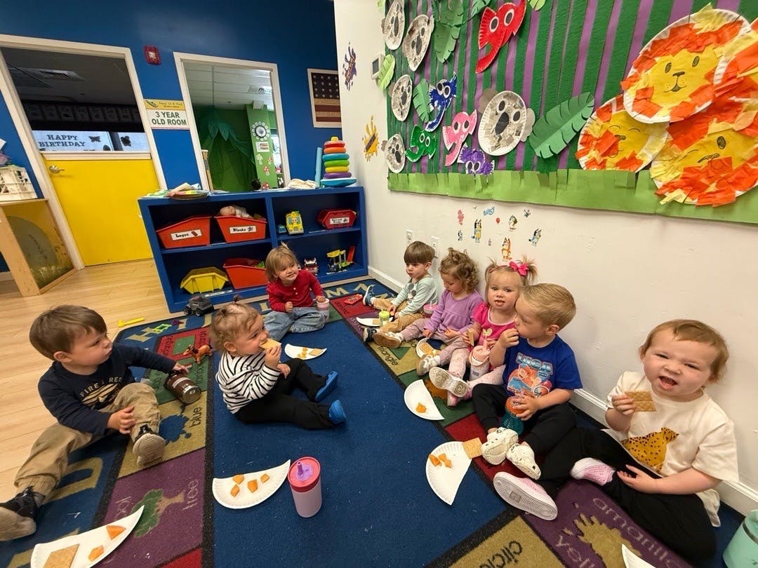 Group of young children sitting on a rug eating snacks in a classroom