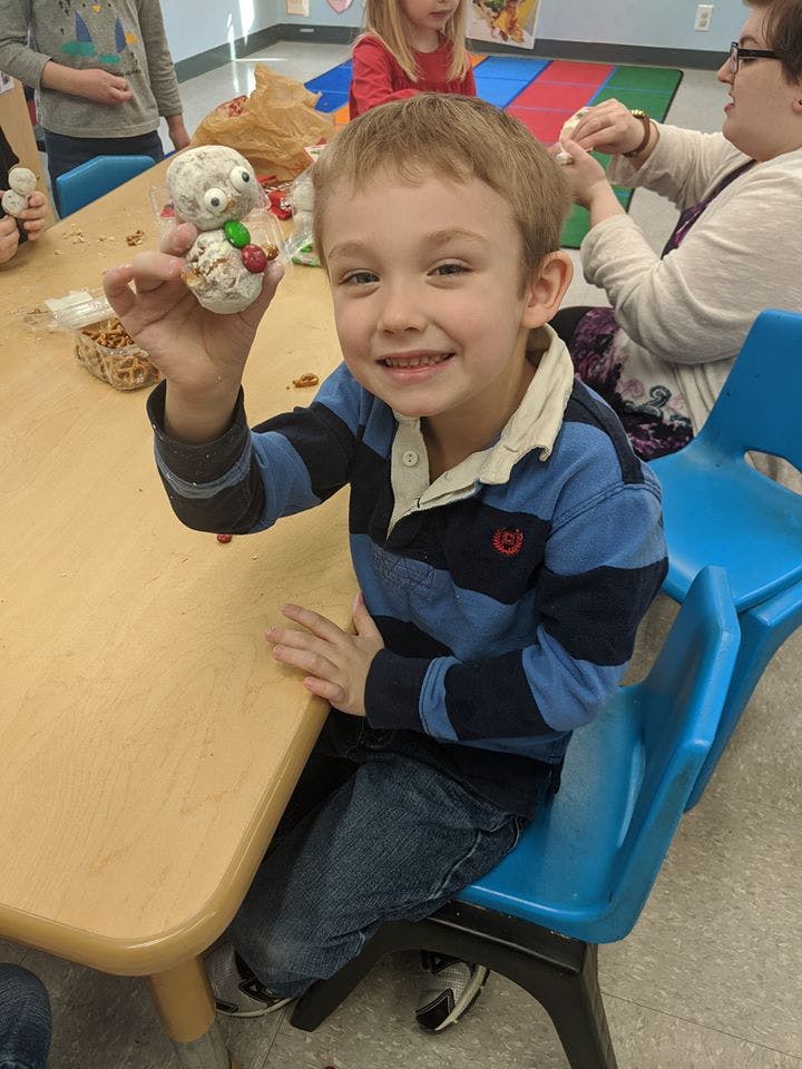 Child holding up a small craft item in a classroom