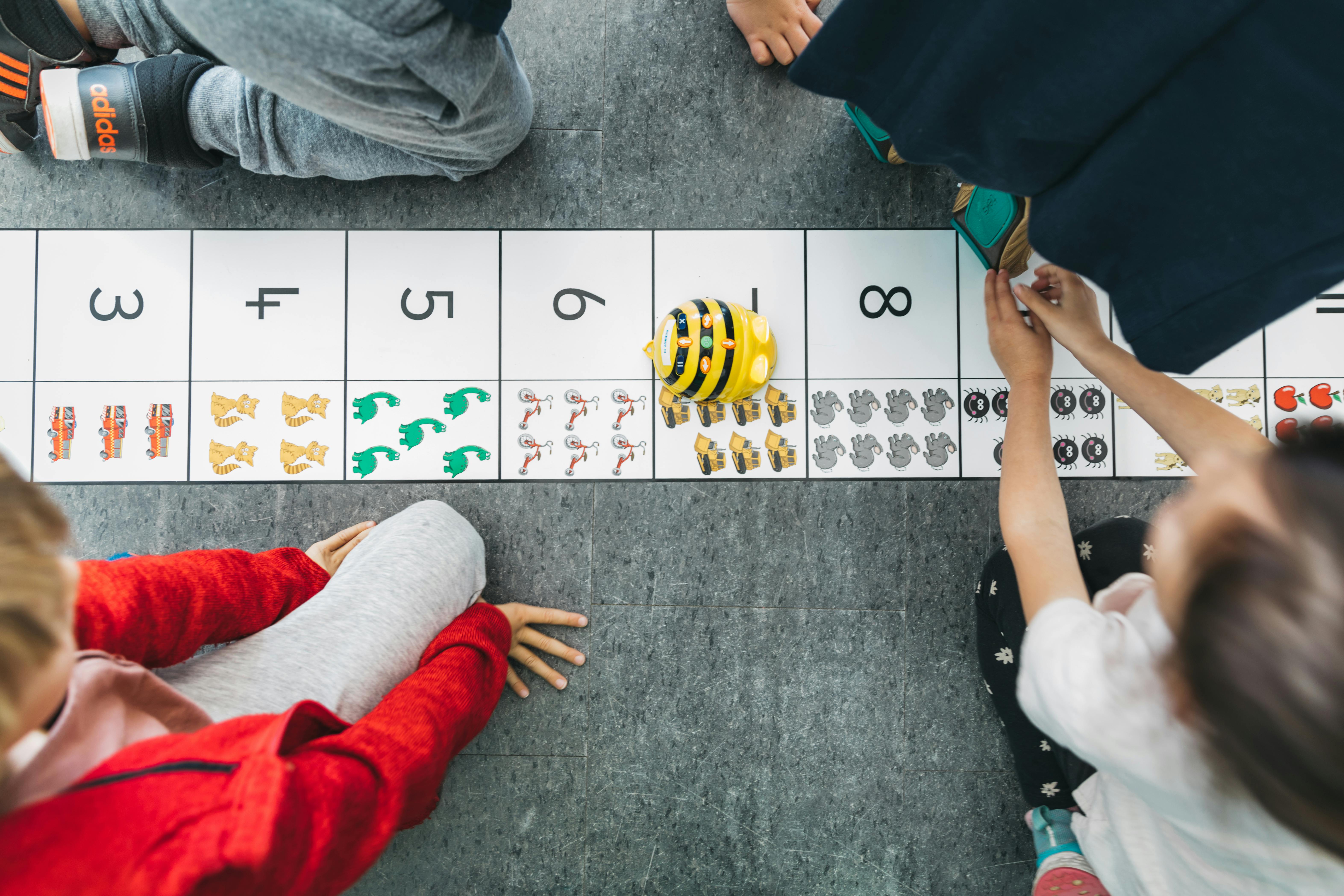 Children playing with a bee-bot on a numbered mat with counting objects mat