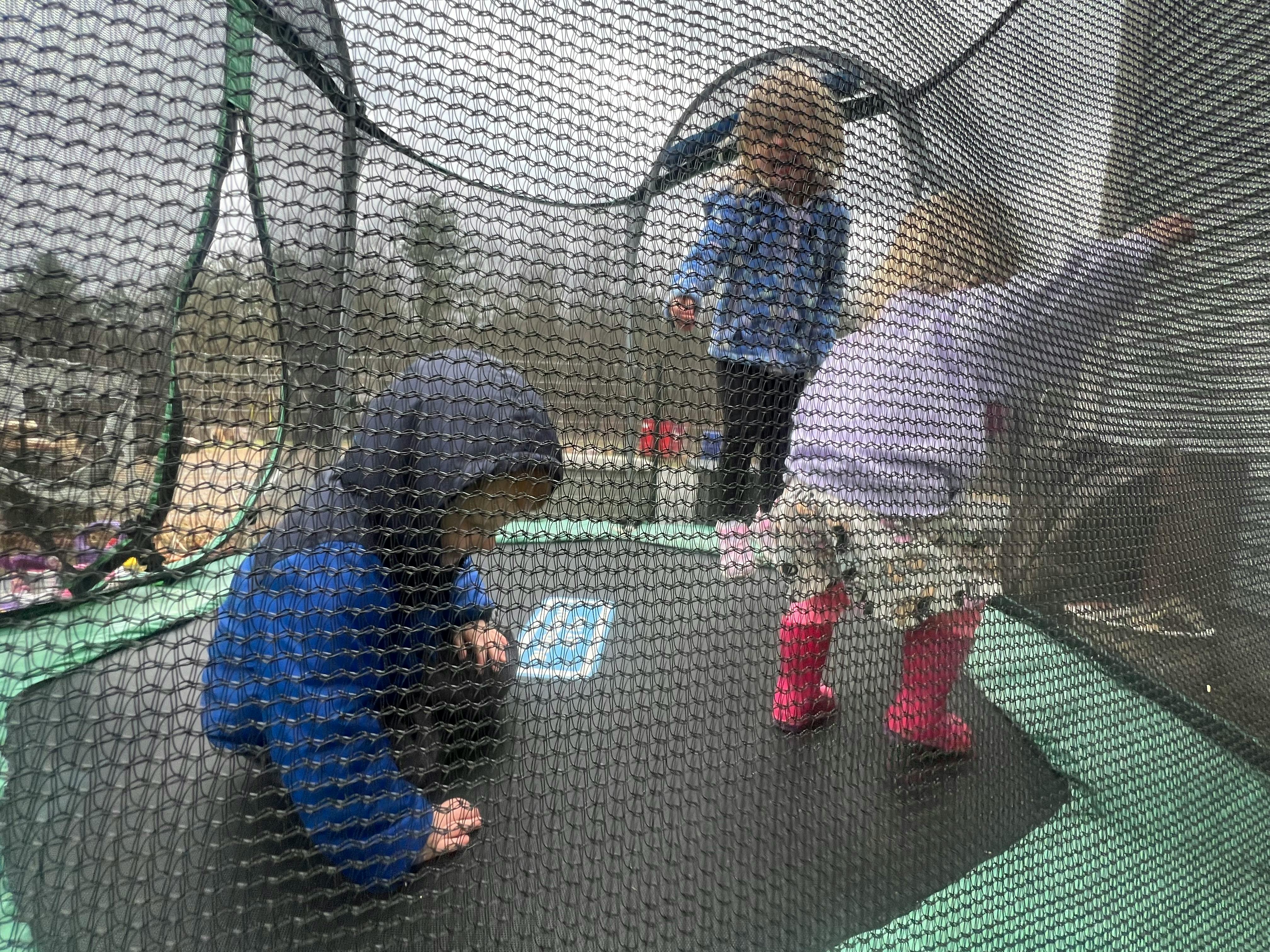 Three children playing on a trampoline with a safety net