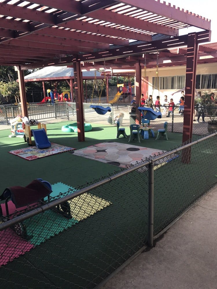 Children on a playground with slides and swings under a wooden pergola
