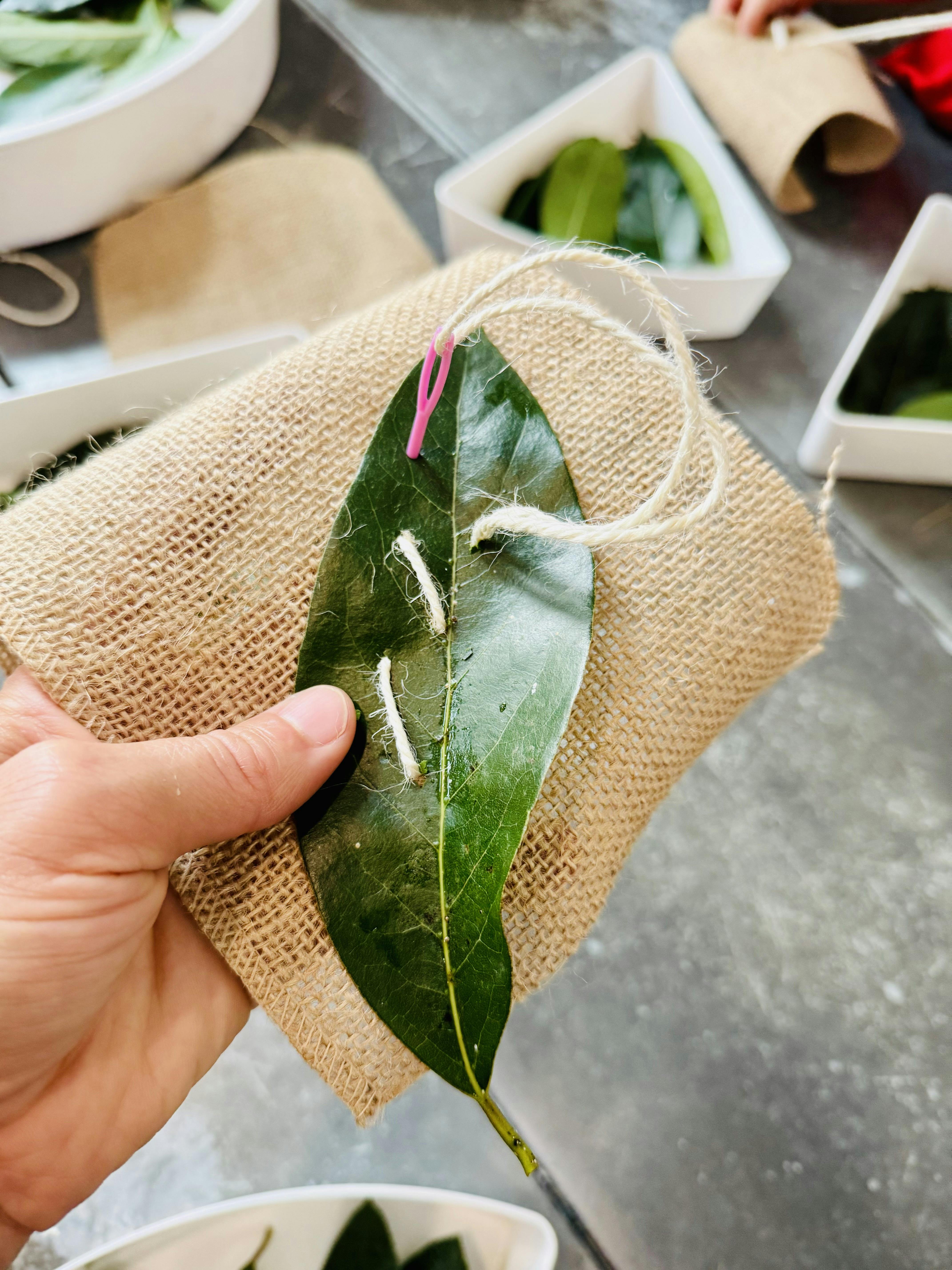 Person holding a leaf with string sewn through it on burlap fabric