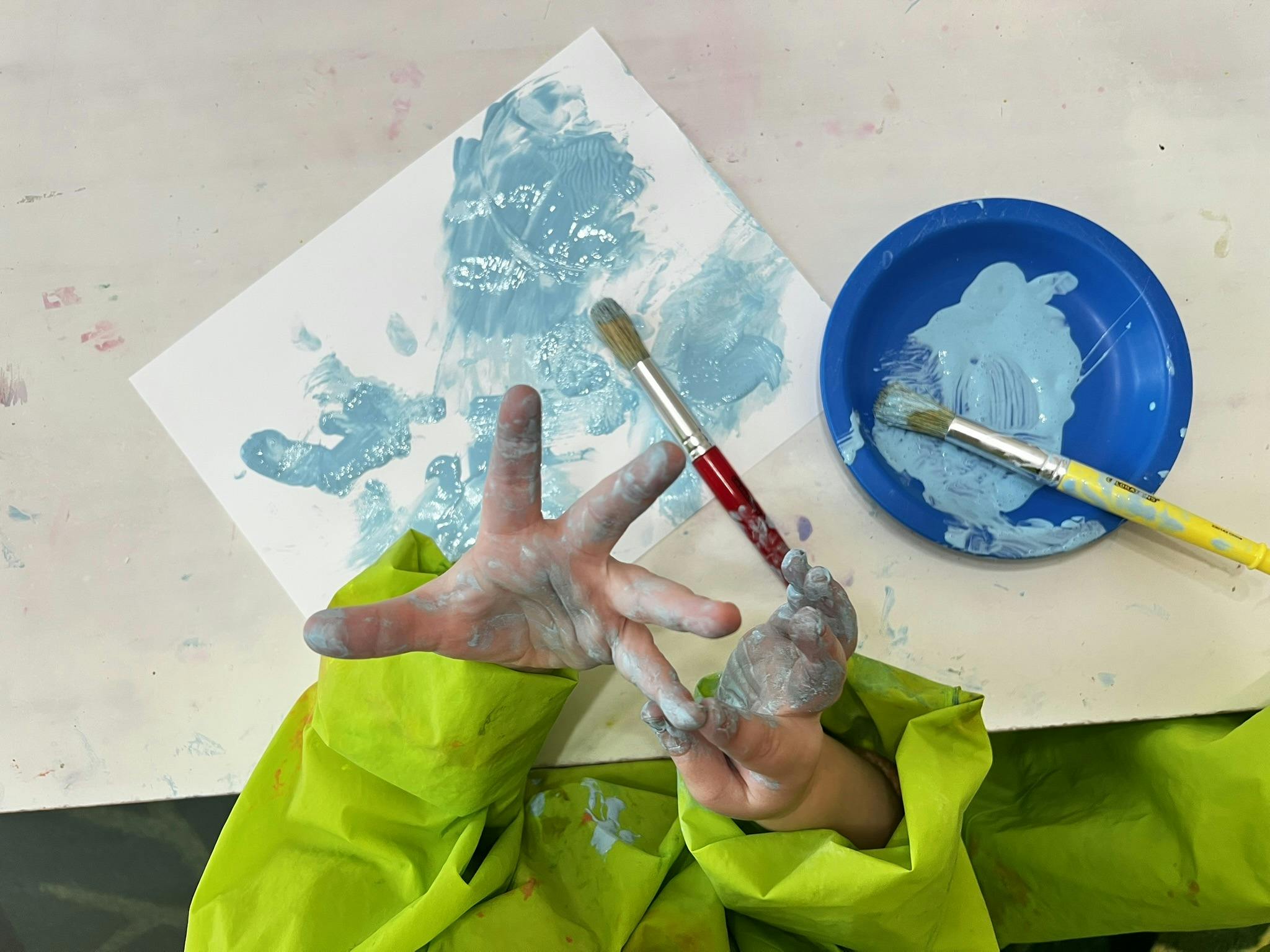 Child's hands covered in light blue paint over a white paper