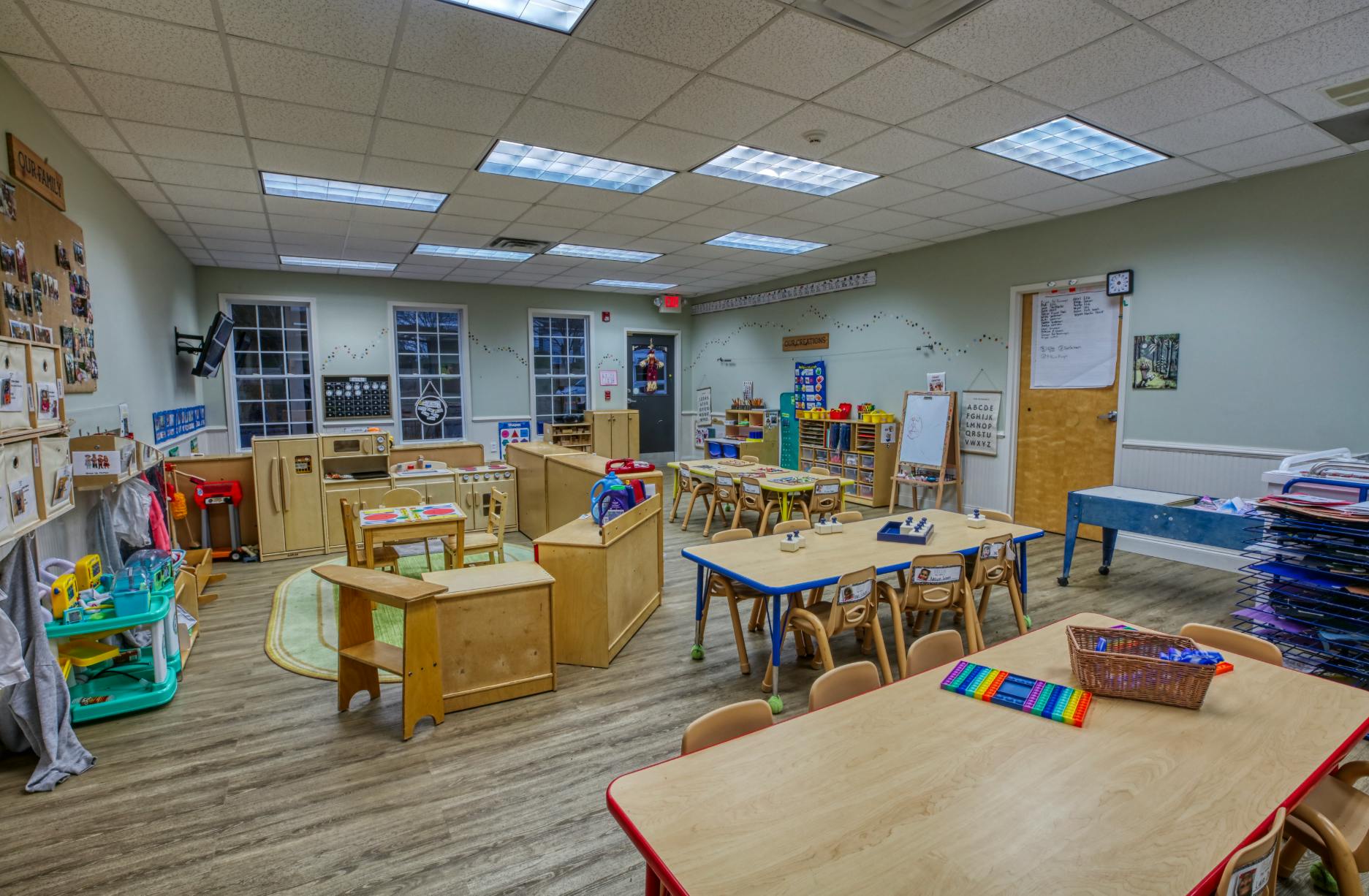 Empty classroom with small tables and chairs, play kitchen, and storage shelves