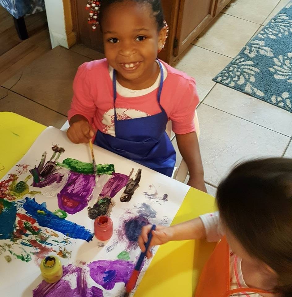 Child in an apron painting on a large sheet of paper