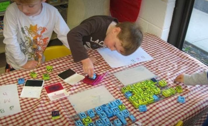 Two children playing with letter tiles and stamps at a table