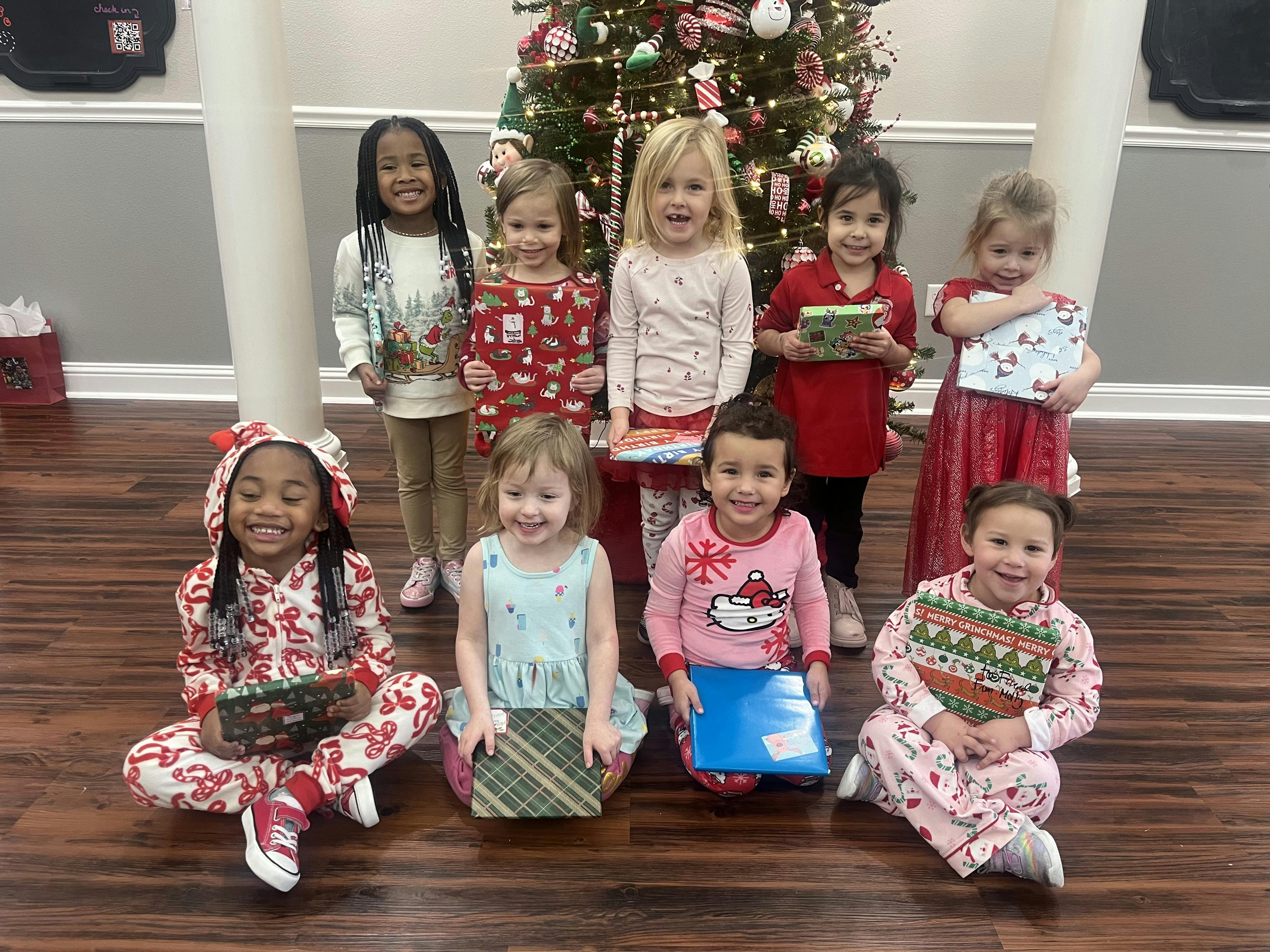 Group of children holding wrapped gifts in front of a Christmas tree
