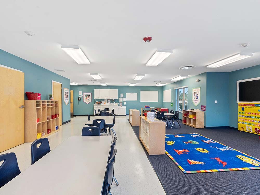 Classroom with tables, chairs, cubbies, and a blue alphabet rug