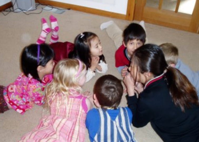 Group of children and one adult sitting on the floor in a circle