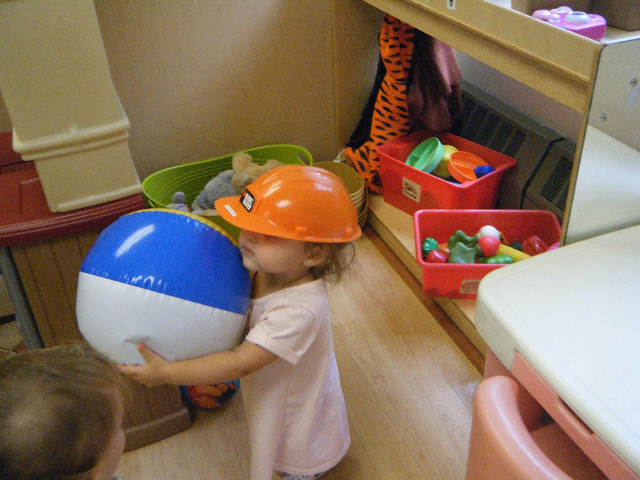 Child wearing an orange hard hat holding a blue and white beach ball
