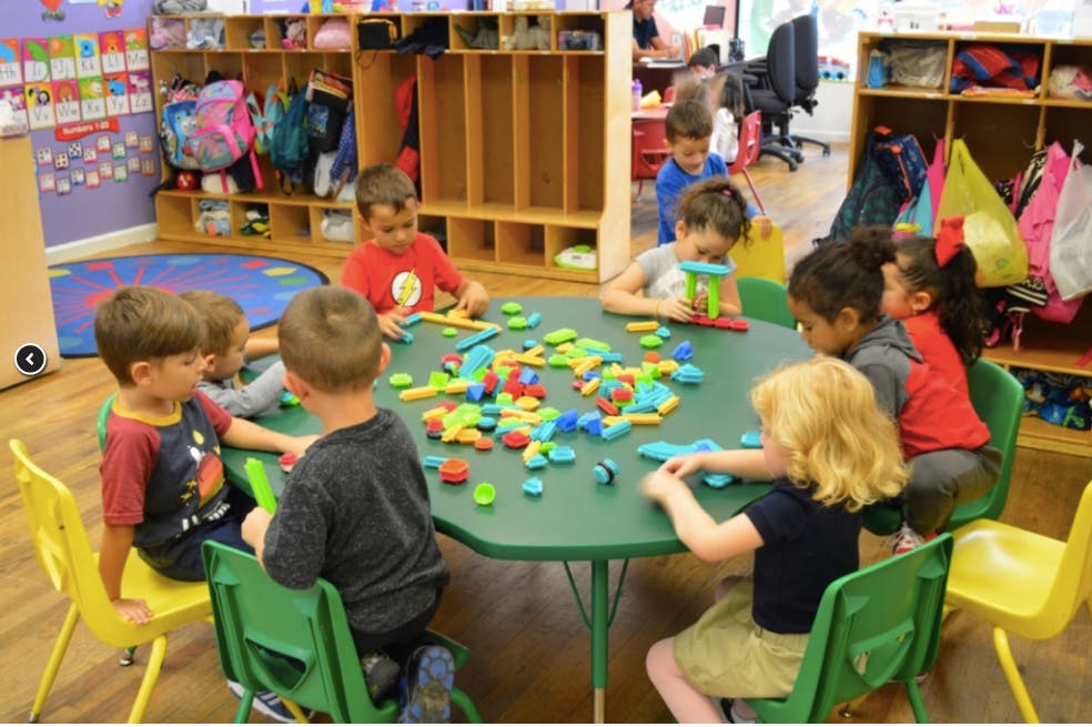 Children playing with colorful building blocks at a table in a classroom