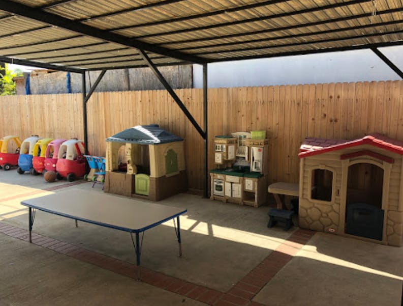 Outdoor play area with toy cars, playhouses, and a table under a canopy