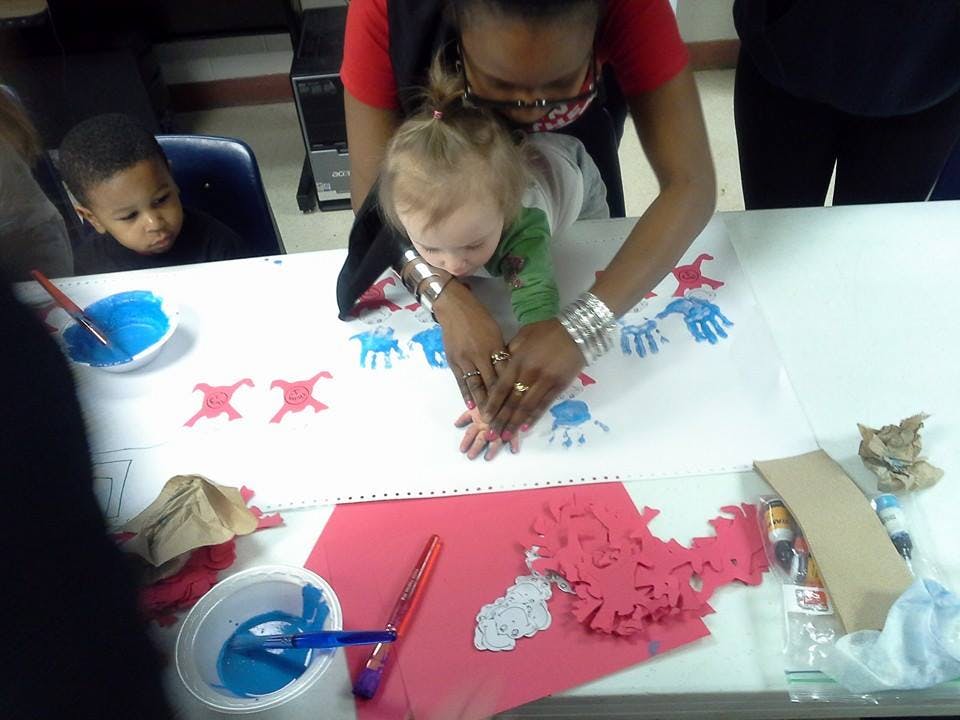 Person helping a child make handprints on paper