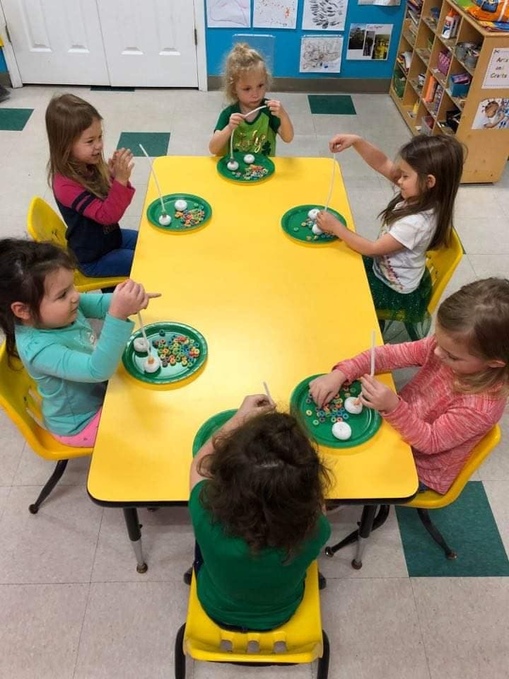 Children sitting at a yellow table doing an activity with plates and small items