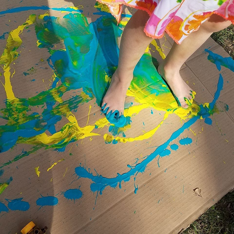 Child's feet covered in blue and yellow paint on cardboard