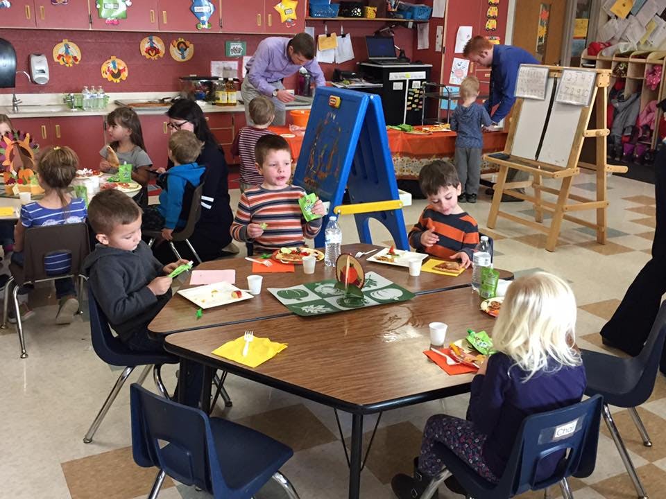 Children and adults in a classroom eating and at tables