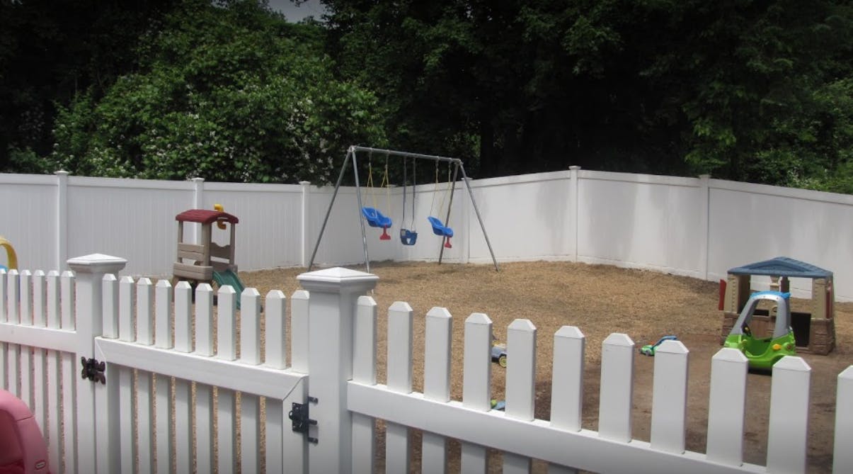 Playground with swings and play structures behind a white picket fence