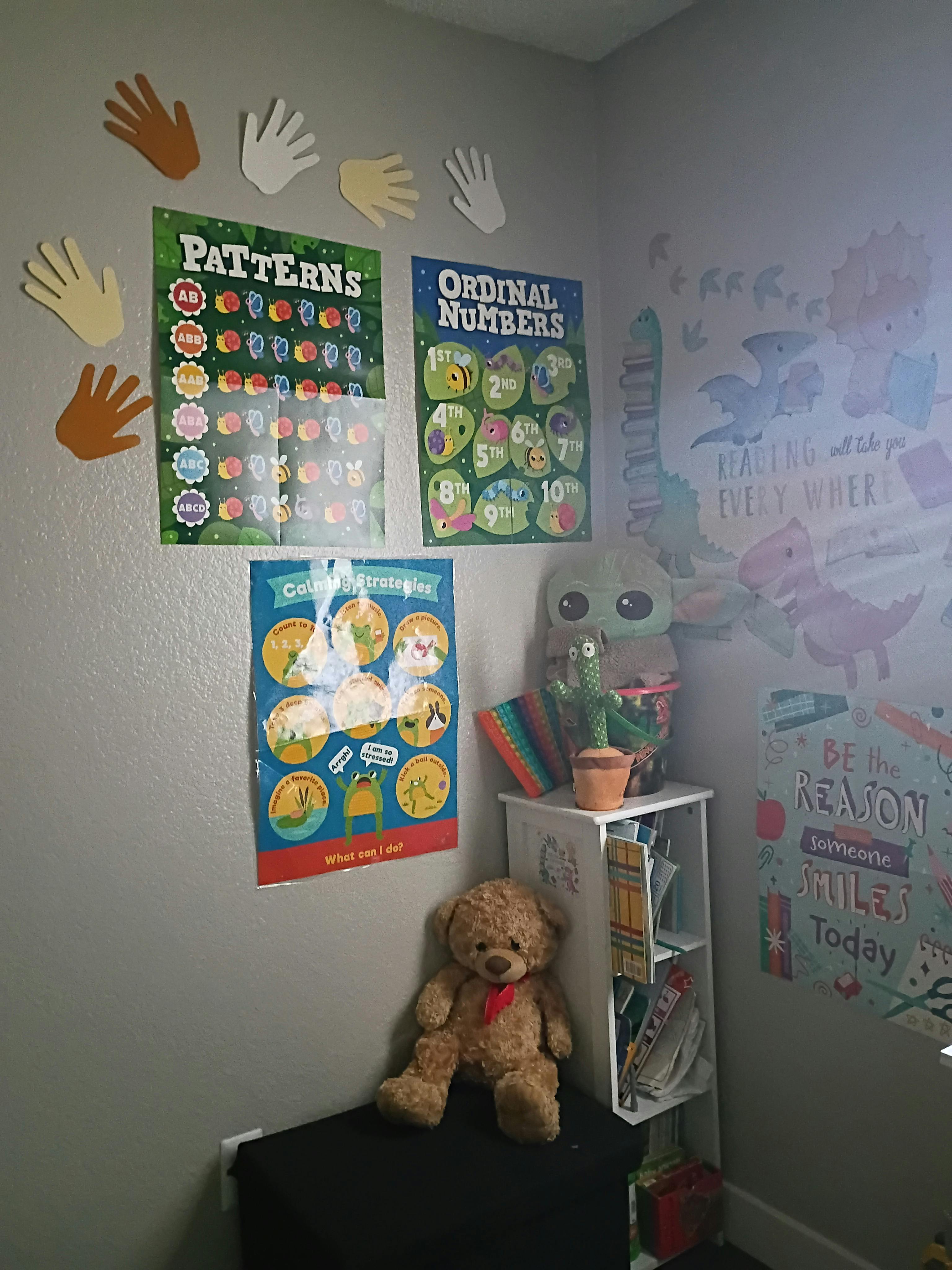 Educational posters and hand cutouts on a wall with toys nearby