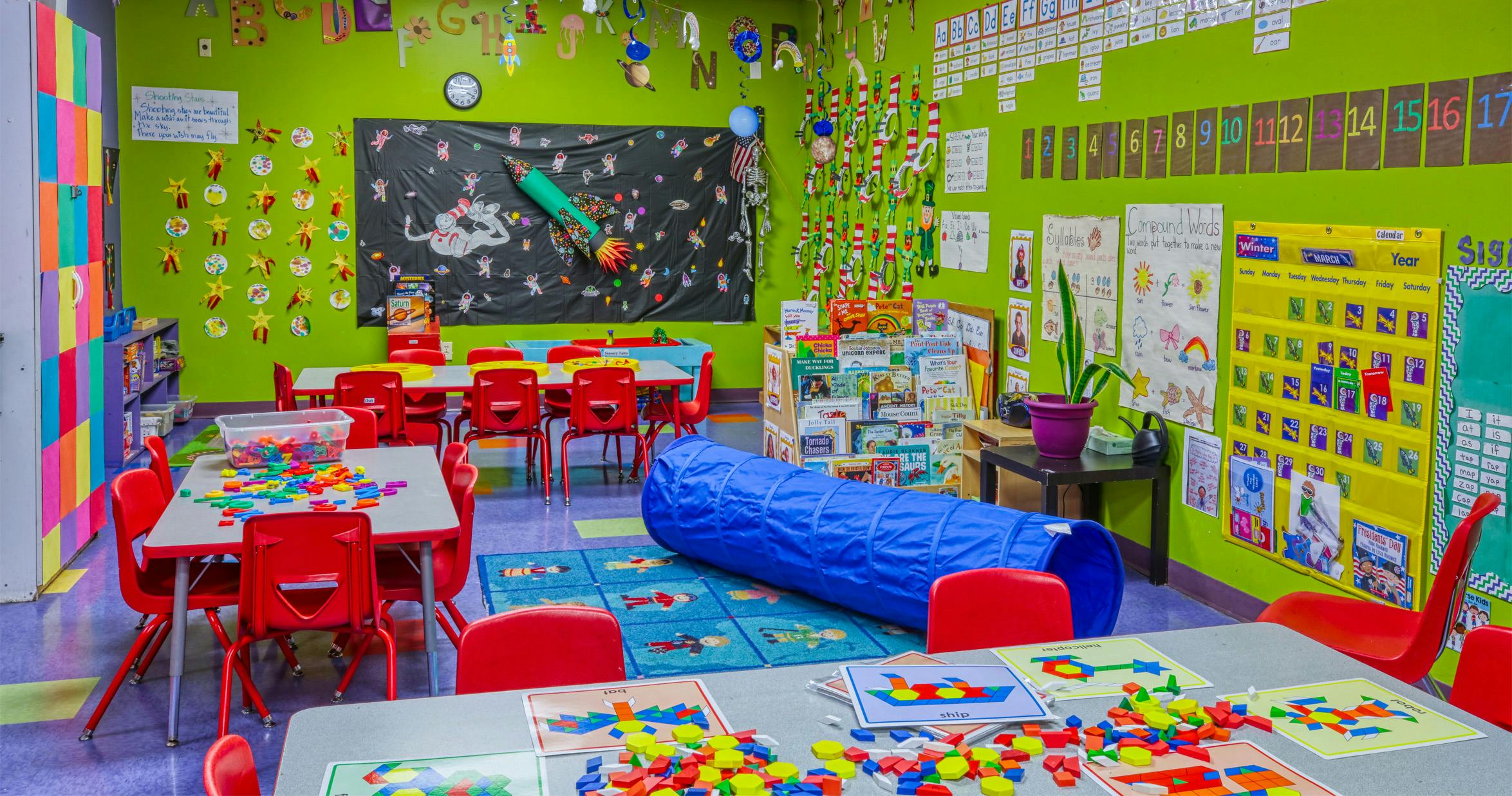 Colorful classroom with red chairs, tables, alphabet and number decorations, and a blue tunnel