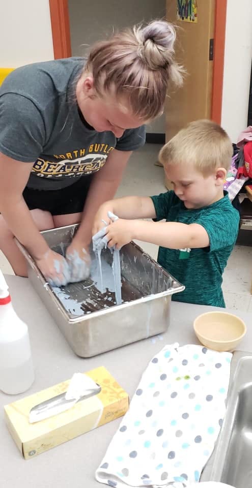 Person and child playing with slime in a metal bin