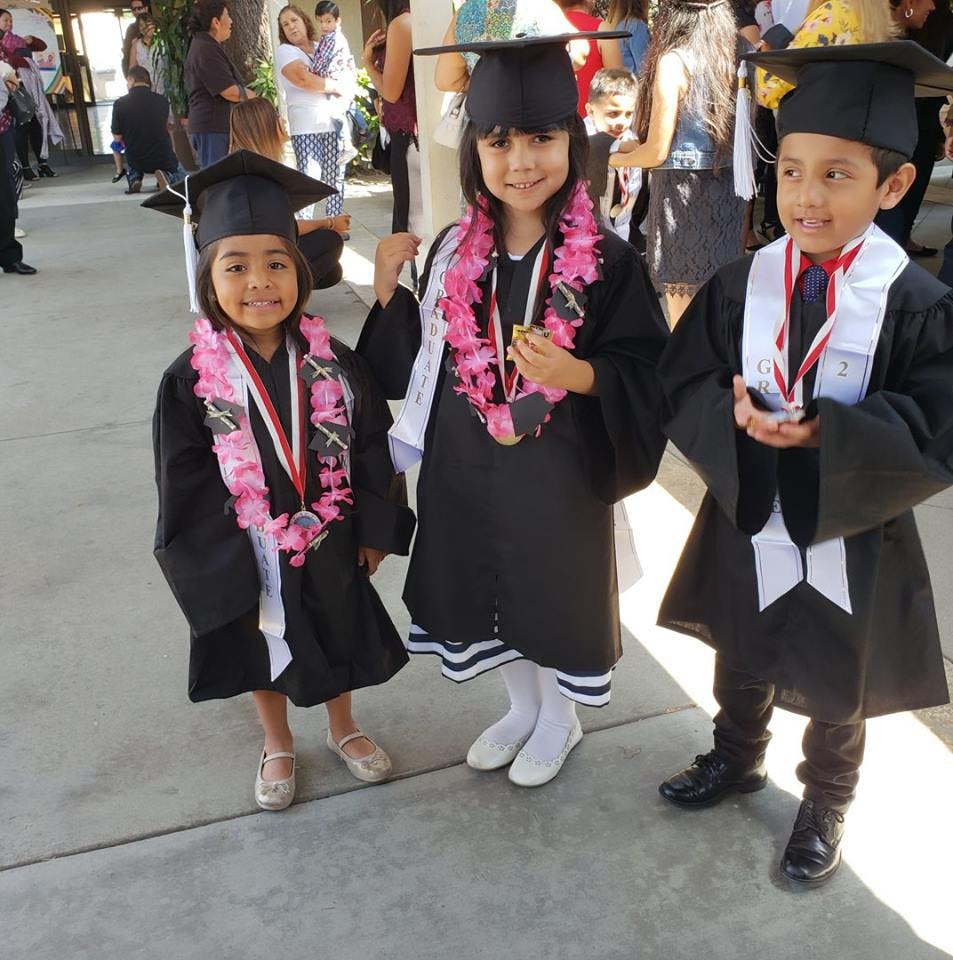 Three children in graduation caps and gowns with leis and medals