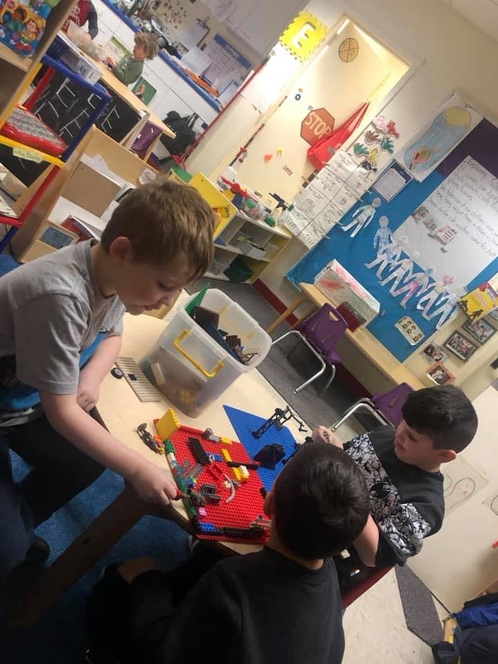 Three children playing with building blocks at a table in a classroom