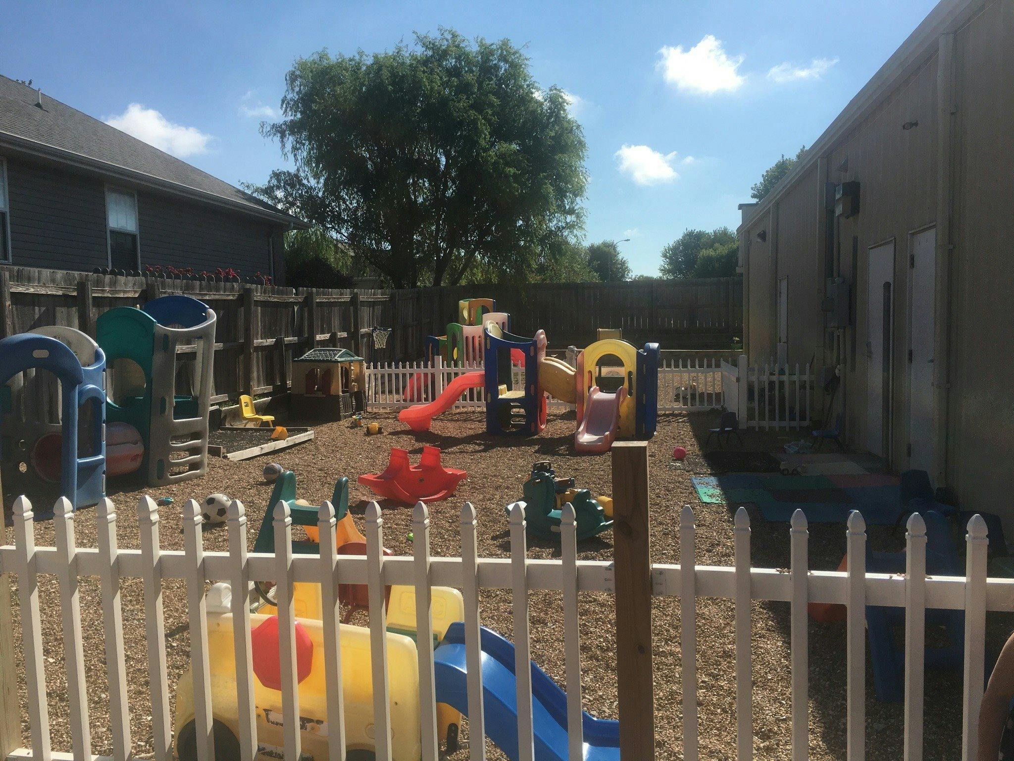 Outdoor playground with various colorful play structures and a white picket fence