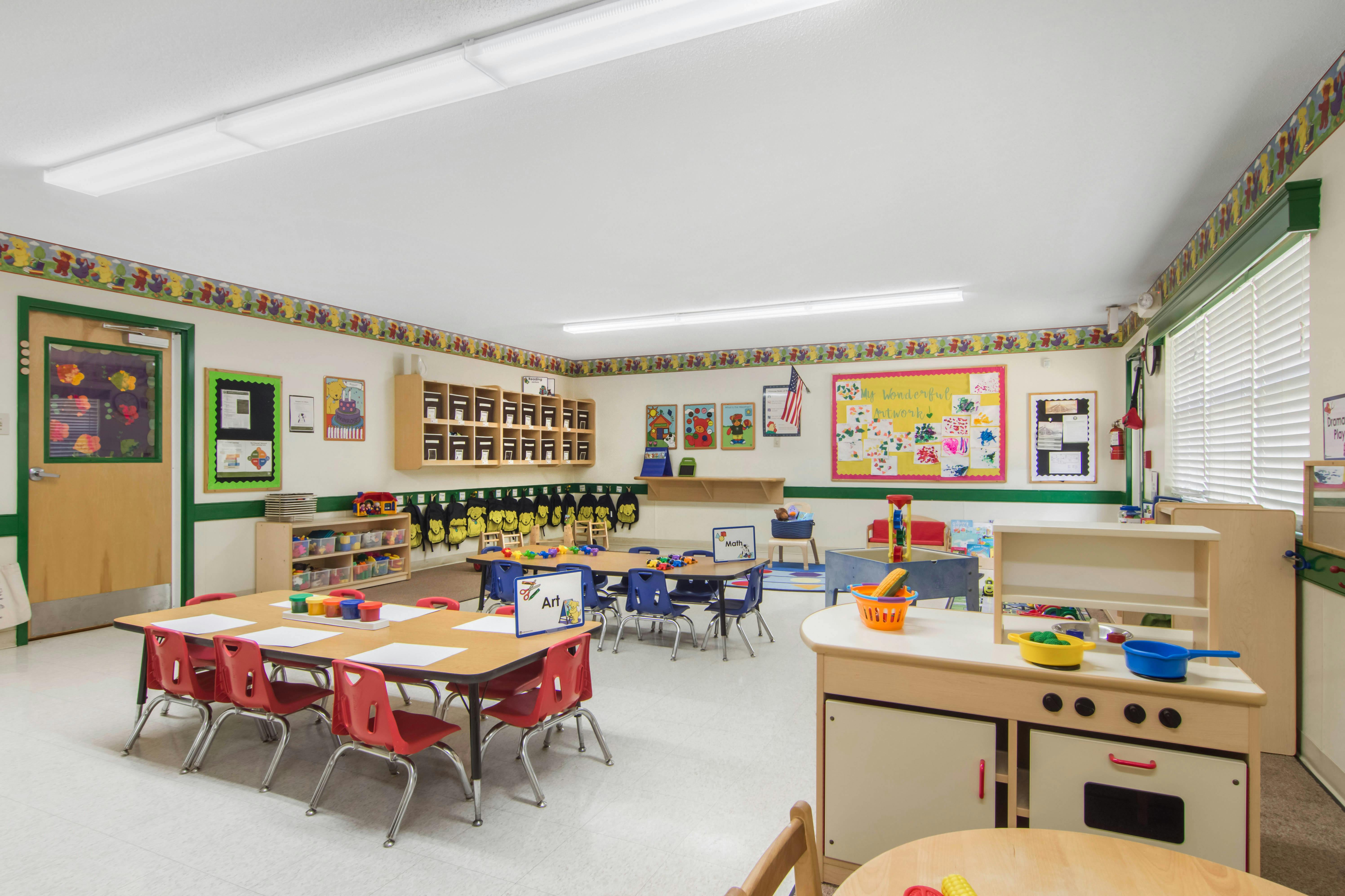 A colorful empty preschool classroom with tables, chairs, and play areas