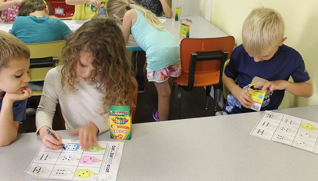 Children at a table, one coloring, another opening a box