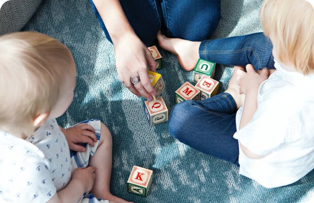 People on a rug playing with alphabet blocks