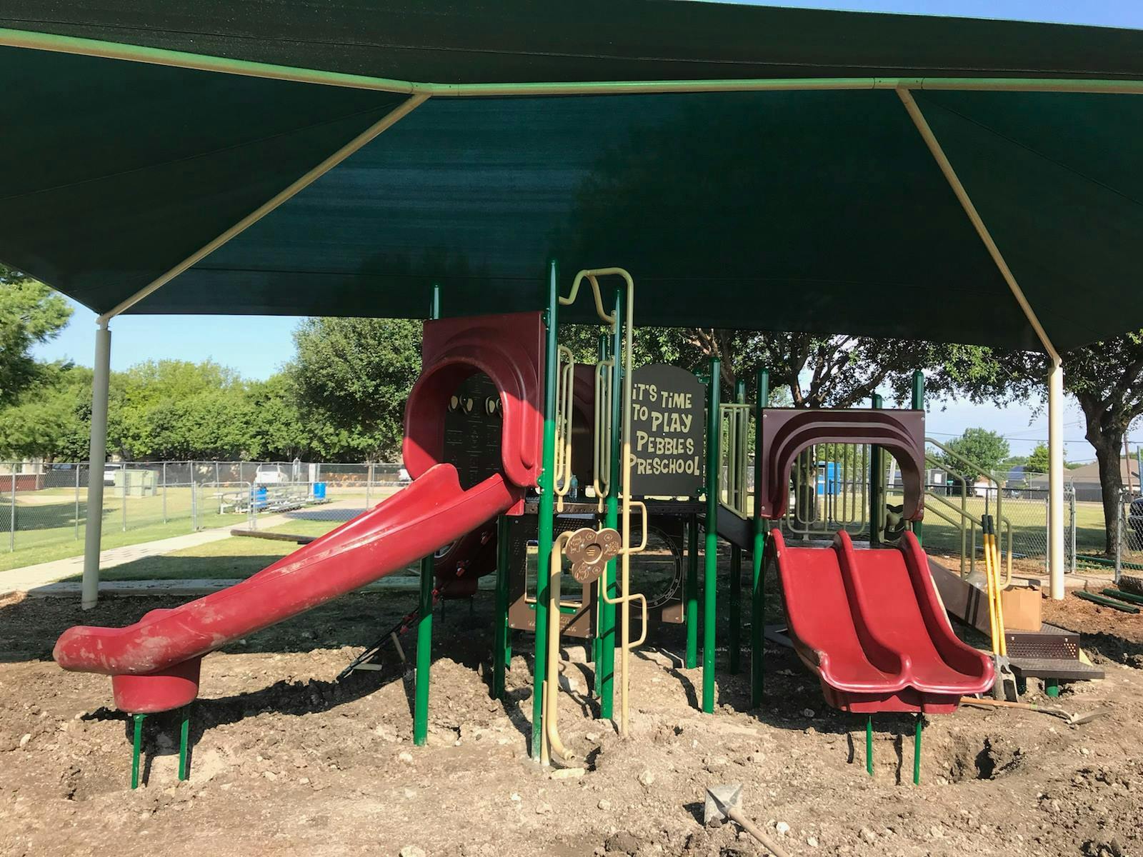 Playground with red slides under a green shade structure
