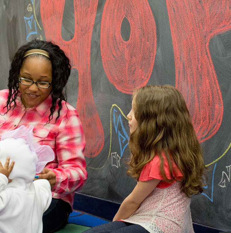 Person interacting with two children in a classroom