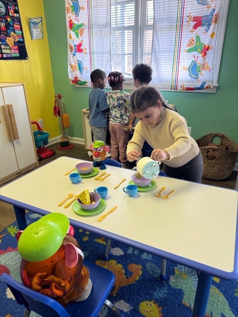 Child playing with toy dishes at a table in a classroom