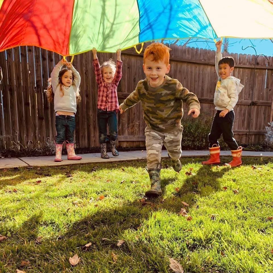 Children playing with a colorful parachute in a grassy backyard