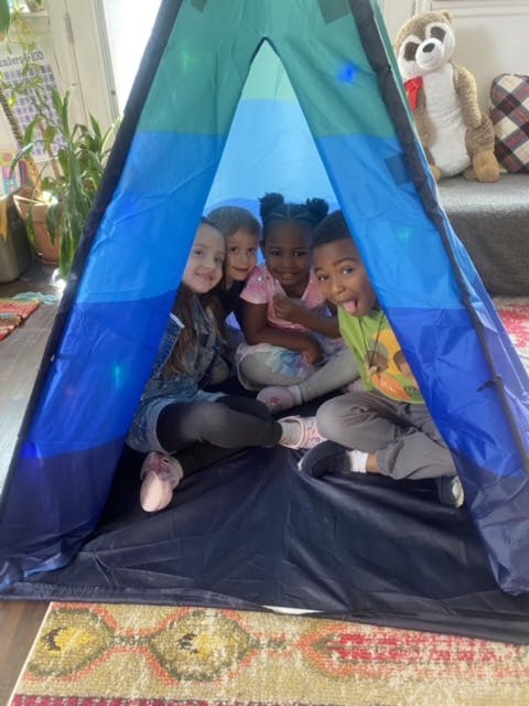 Four children sitting inside a blue and green play tent