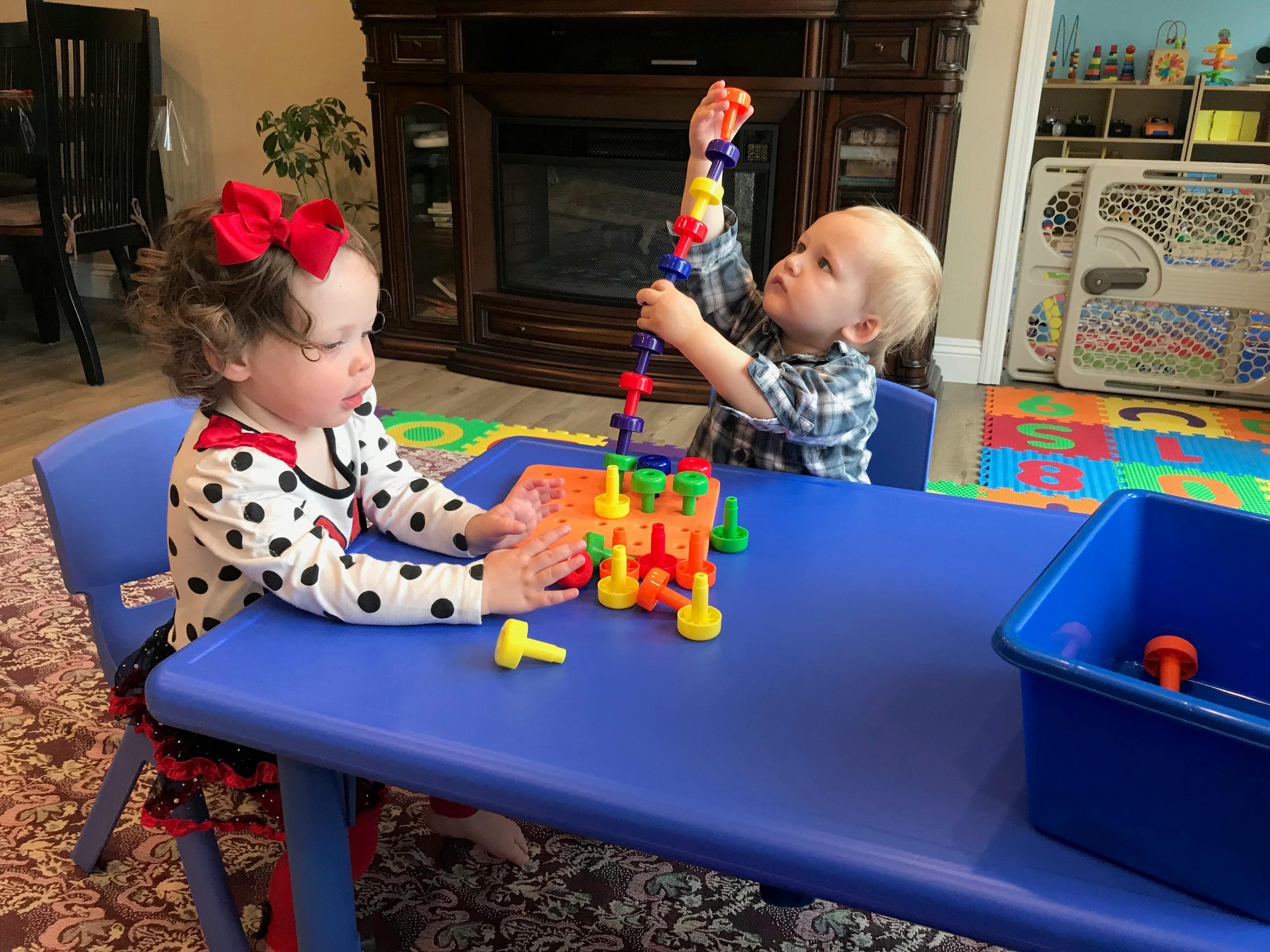 Two children playing with colorful building toys at a blue table
