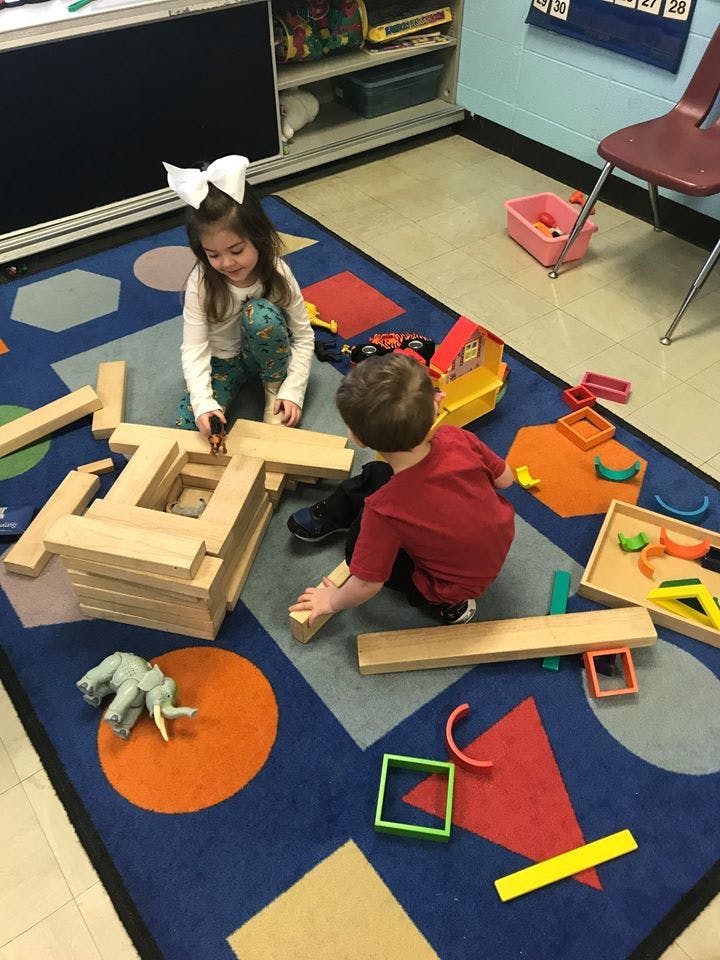 Two children playing with wooden blocks on a colorful rug